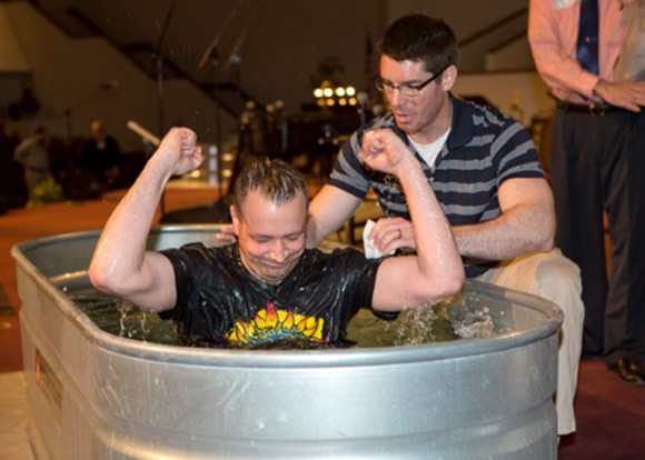 After being baptized in a horse trough, David Vittetoe celebrates as John Howard, minister to students, assists. The troughs gave the church three locations to baptize the 103 people who came forward.