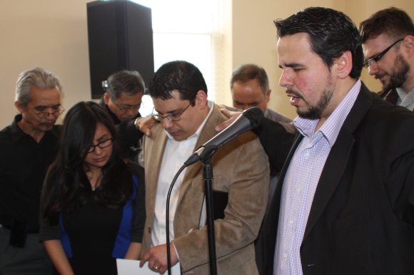 Starting Point in Chicago: Pastor Marvin del Rios of Iglesia Bautista Erie (right) prays for the new congregation his church is sponsoring, led by Pastor Jonathan de la O and his wife, Emely, surrounded by leaders from Chinese, Korean, and Romanian church plants who attended the April 6 launch service.