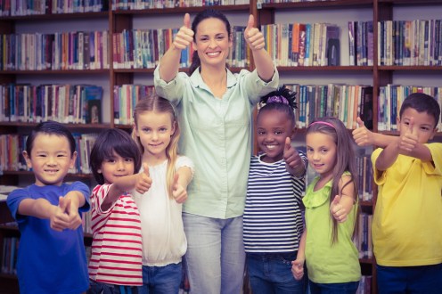 Pupils and teacher smiling at camera in library at the elementary school
